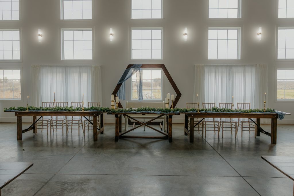 A traditional wedding head table setup with a long rectangular table, elegantly decorated with floral arrangements, seating the wedding party on one side facing the guests.